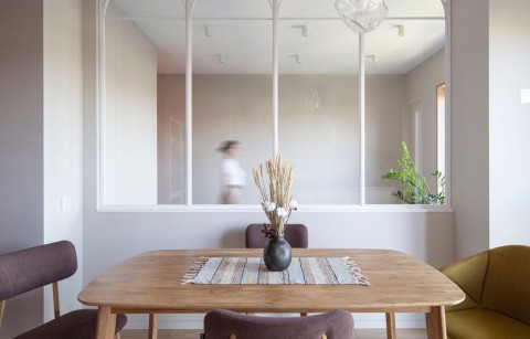 Terra Apartment dining table facing an arched glass partition between living room and kitchen