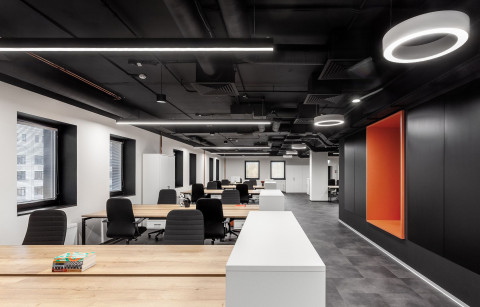 UNICA Office open workspace with black ceiling, wood desks and orange wall niche