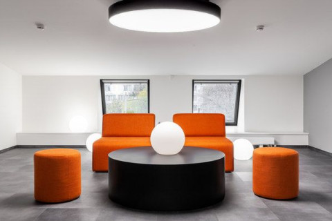 UNICA Office lounge area with orange sofas, round black table and globe lights