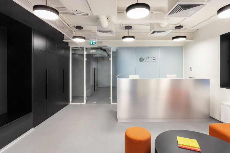 UNICA Office reception area with metal desk, black storage wall and orange lounge seating